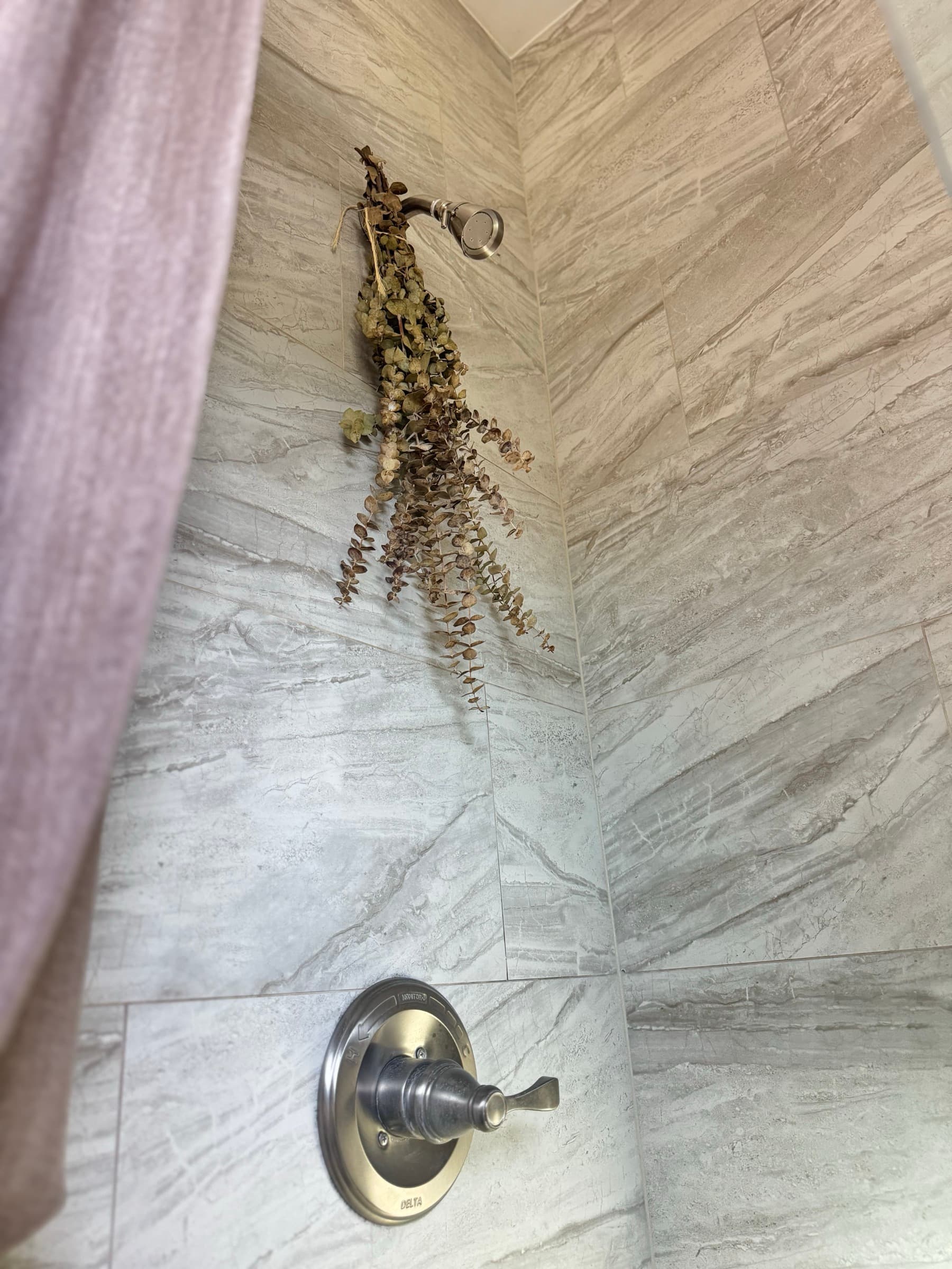 Marble-look tiled shower with eucalyptus hanging from the showerhead