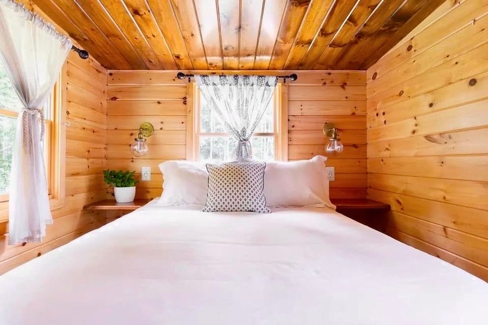 Stand-up bedroom with full bed, wood walls, and bedside sconces